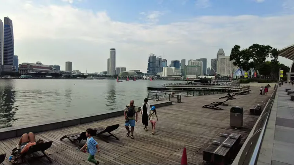 Family walking on Singapore boardwalk with skyline and lounge chairs